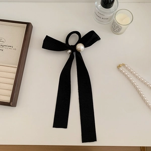 Chouchou élégant à nœud en ruban noir avec perles blanches sur un fond de coiffeuse