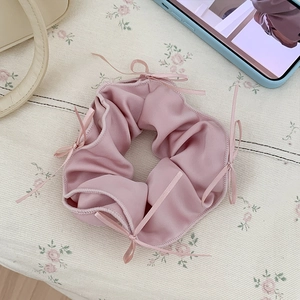 Detail of pink satin scrunchie with delicate ribbon bows on a floral background