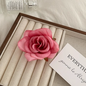Detailed top view of a pink faux rose hair claw clip on a beige velvet jewelry tray