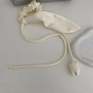 Dettaglio dell'elastico in raso crema con lunghi nastri e ciondoli a tulipano