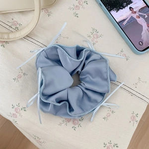 Detail of blue satin scrunchie with delicate white ribbon bows and soft fabric texture