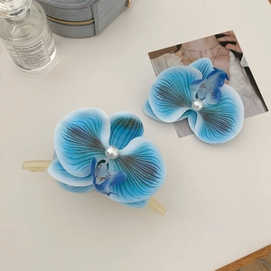 Detail von blau verlaufenden Orchideen-Haarspangen mit weißen Perlen auf weißem Tisch