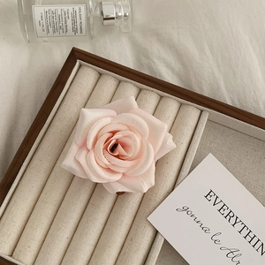 Detailed close-up of a pink faux rose hair claw clip resting in a wooden jewelry organizer