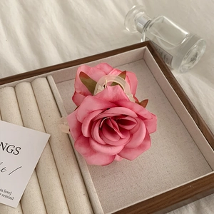 Detail of a pink silk rose hair claw clip displayed on a wooden jewelry tray with perfume