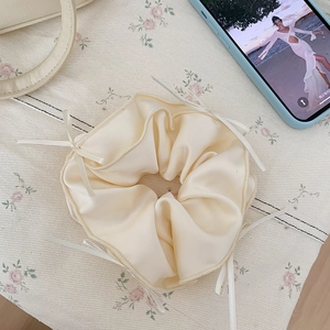 Close-up of cream satin scrunchie with delicate ribbon bows on floral fabric