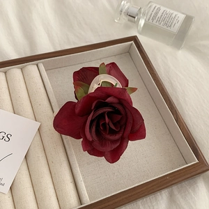 Detail of dark red fabric rose hair claw clip with green leaves on a jewelry tray