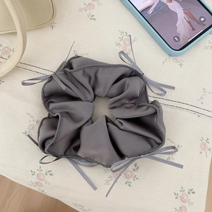 Detail of dark grey satin scrunchie with ribbons on minimalist floral background