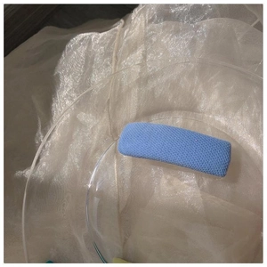 Minimalistische hellblaue Haarklammer mit Stricktextur auf Glasteller und Organza-Stoffhintergrund