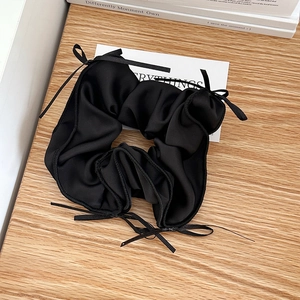 Detail of black silk satin hair scrunchie with delicate ribbon bows on wooden desk