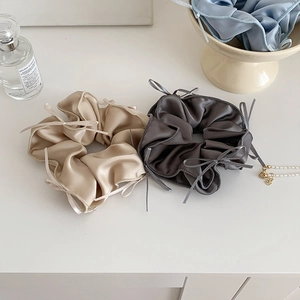 Close-up of beige and dark grey satin scrunchies with elegant ribbon bow details