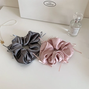 Close-up of pink and grey silk scrunchies with delicate ribbon bows on white surface
