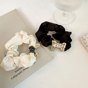 Detail of satin scrunchies with golden metal bow and crystal stone in cream and black