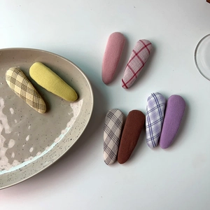 Detail showing eight pastel fabric-covered snap hair clips in solid and plaid patterns