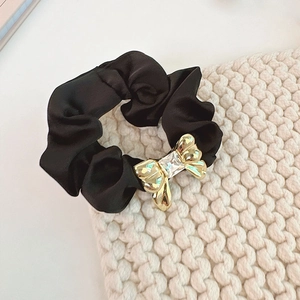 Detail of black satin scrunchie with a gold metal bow and sparkling crystal decoration