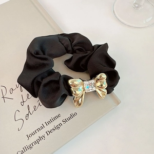 Close-up of black satin scrunchie with a gold metal bow and sparkling crystal center