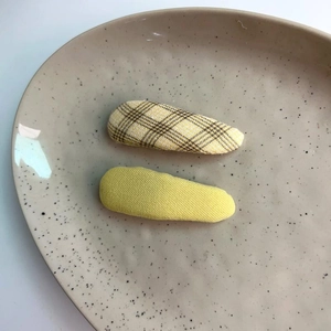 Set of two plaid and yellow fabric BB hair clips displayed on a ceramic dish