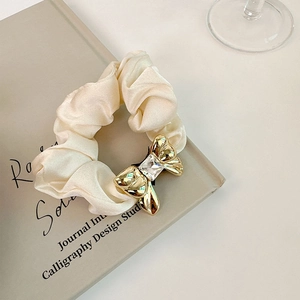 Detail of cream satin hair scrunchie with golden metal bow and sparkling crystal stone