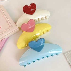Three oversized hair claws in beige, yellow, and blue with colorful 3D heart accents