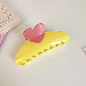 Macro detail of large yellow hair claw clip with pink heart decoration and glossy finish