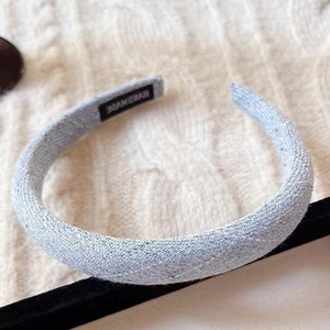 Detail of light blue tweed padded headband with a handmade label on soft knit background