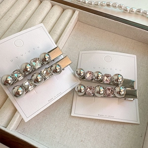 Détail de quatre barrettes à boules argentées et strass sur une carte blanche
