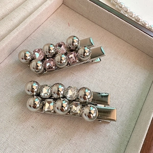 Détail de barrettes argentées avec cristaux roses et transparents sur tissu beige