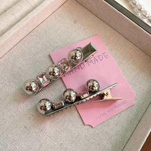 Détail de barrettes argentées avec cristaux roses et perles sur carte en cœur