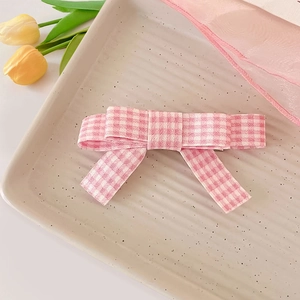 Détail d'une pince à cheveux à nœud vichy rose sur un plateau avec des fleurs