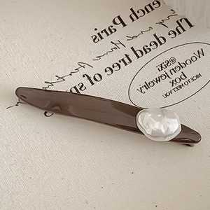 Barrette à cheveux marron avec perle baroque sur fond texturé, style minimaliste