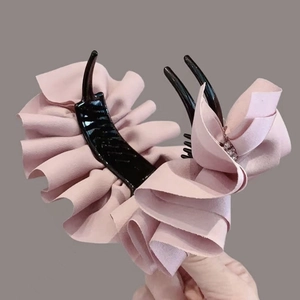 Pince à cheveux rose en tissu plissé avec strass brillants tenue à la main
