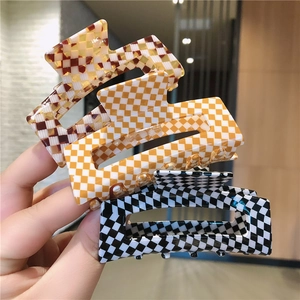 Détail de grandes pinces à cheveux en acétate aux motifs de damiers noir orange et marron
