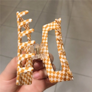 Détail d'une grande pince à cheveux carrée en acétate avec motif damier orange et blanc