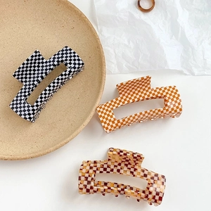 Trois pinces à cheveux en acétate à motif damier noir, orange et marron sur un plateau