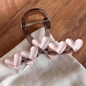 Pince à cheveux en résine brune avec cœurs roses 3D posée sur un tissu en lin blanc