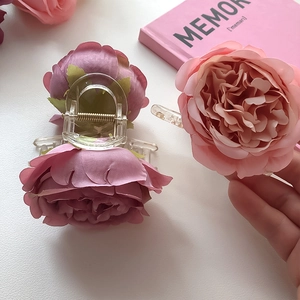 Detail of a pink silk rose hair claw clip with layered fabric petals and clear grip
