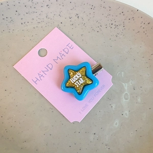 Detail of glittery blue lucky star hair clip on a decorative pink display card
