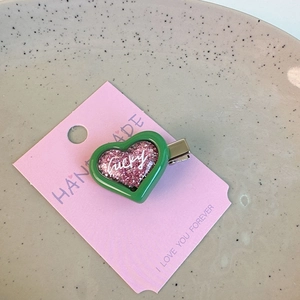 Close-up of a Y2K candy heart hair clip with pink glitter and lucky text on a ceramic plate