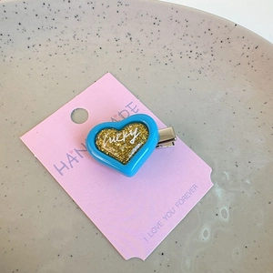 Close-up of blue resin heart hair clip with gold glitter and white lucky script detail