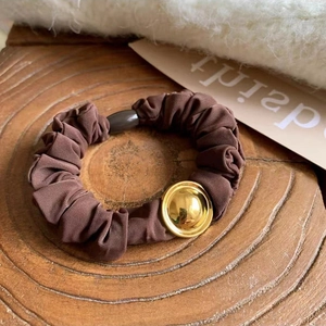 Detailed macro view of a brown pleated hair scrunchie with a gold metal buckle detail