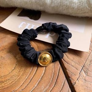 Detail of black fabric hair tie with golden metal buckle on a wooden surface