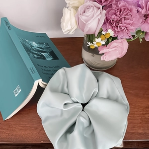 Elegant mint green satin scrunchie placed on wood with fresh flowers and magazine