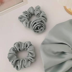 Detail of sage green satin scrunchie with 3D rose flower and pleated fabric texture