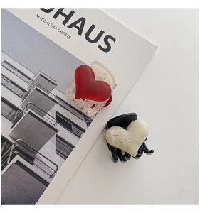 Détail de pinces à cheveux coeur rouge mat et marbre sur un magazine de mode