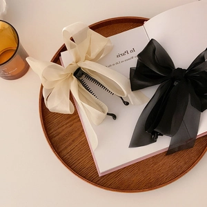 Detail of chiffon bow banana hair clips in cream and black on a vintage wooden tray