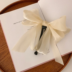 Detail of cream chiffon bow banana clip on book page, elegant ponytail hair accessory