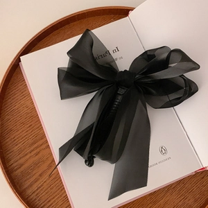 Detail of elegant black oversized chiffon bow hair clip resting on an open vintage book