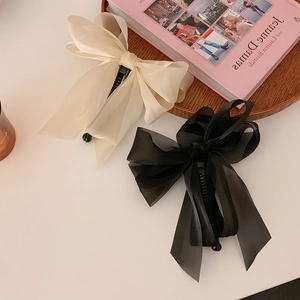 Macro view of large chiffon bow banana clips in cream and black on a white surface
