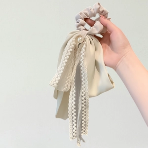 Elegant cream silk scrunchie with lace ribbons and pearl detail held in hand