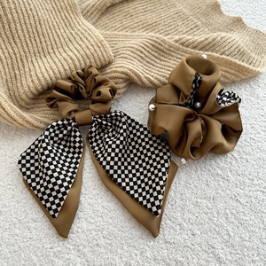 Detail eines karierten braunen Satin-Haargummis mit eleganten Perlen auf Strickstoff