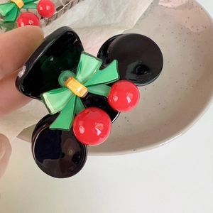 Detail of a black resin hair claw featuring red cherry charms and a green bow accent